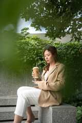 Business asian woman drinking coffee outside city building use smartphone internet connection - 749190239