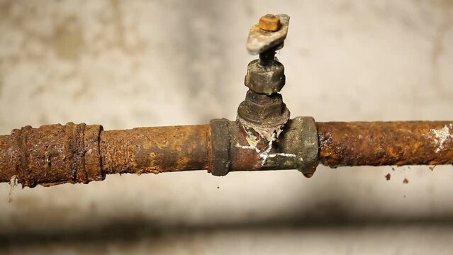 An old water tap leaks along a rusty water pipe. The water pipe in the basement is covered in rust. Cyclic, endless.