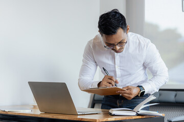 Fototapeta premium Happy middle aged business man ceo wearing suit standing in office using digital tablet. Smiling mature businessman professional executive manager looking away thinking working on tech device.