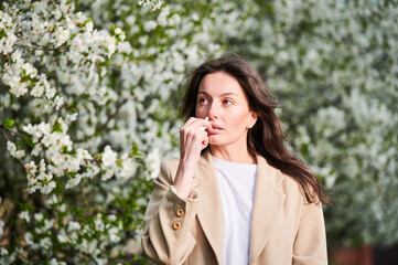 Woman allergic using medical nasal drops, suffering from seasonal allergy at spring in blossoming...