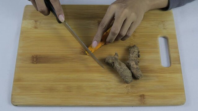 Close up view of Asian woman slicing turmeric (Curcuma longa) on wooden cutting board