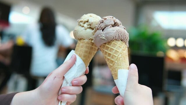 Two servings of ice cream cone on background of Mall, two girls clinking together with a brown, like glasses, game of communication, Friendship, eating delicious dessert. chocolate ice cream