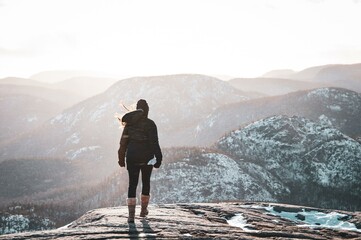 Standing atop the snow-capped peak, a lone woman gazes out into the distance - obrazy, fototapety, plakaty