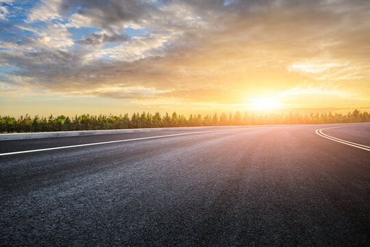 Empty asphalt road and woods under sunset light