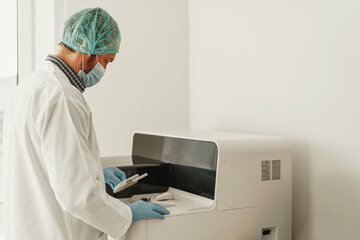 Male scientist in uniform and mask putting a small plastic test tube in a microcentrifuge