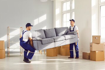 Two young moving service employees workers carrying heavy sofa together in the living room. Men...
