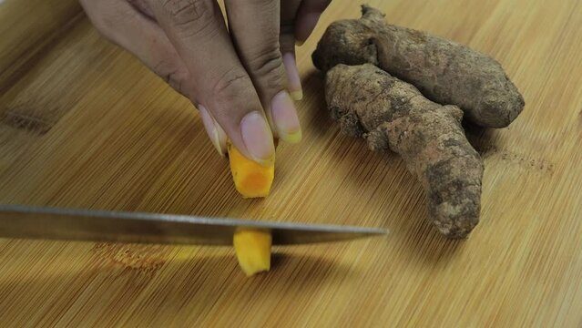 Close up view of Asian woman slicing turmeric (Curcuma longa) on wooden cutting board