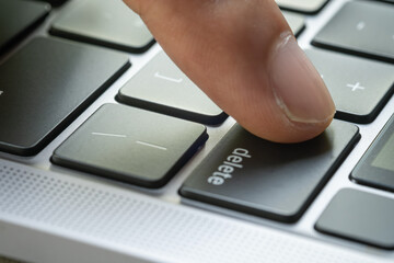 Finger of the computer user, he presses the delete button on the computer keyboard.
