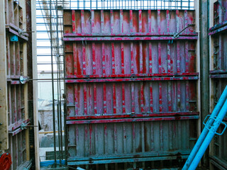 A construction site with a red wall and a blue pipe. Scene is industrial and rugged