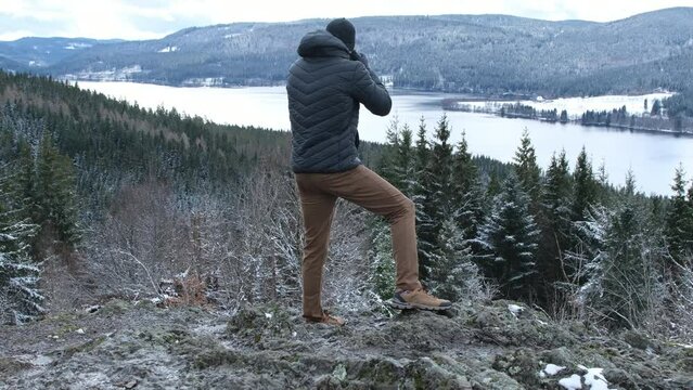 a photographer man on the top of the mountain is taking photos of the lake and winter forest