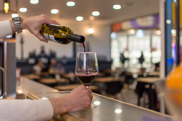 Waiter pouring wine in glass. Sommelier with bottle of red wine. Tasting wine in restaurant.