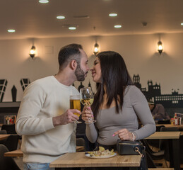 Beautiful couple drinking beverages and having fun in restaurant. Gorgeous young woman and handsome man sitting, laughing and holding glasses of white wine and beer in hands.