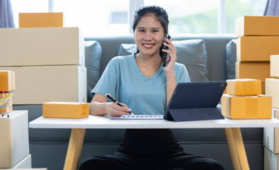 Young Asian woman starting an online selling business at home using mobile phone is checking online...