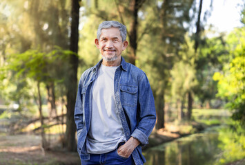 Obraz premium portrait asian senior man with grey hair and beard standing in the forest park,mature male travel in nature,concept of elderly pensioner lifestyle,holiday,travel,camping,relaxation