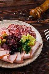 Meat plate with slices of sausage, ham, bacon, olives, spices and greens.