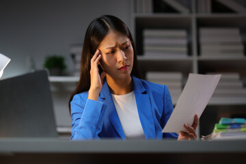 Young Asian businesswoman working with work document paperwork during the night, working overtime...