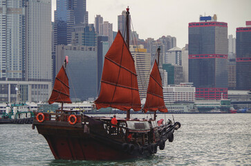 Traditional Chinese junk with red sails and Hong Kong Hongkong skyline in Victoria Harbor with marine traffic, boats, tugs and skyscraper skyline