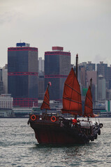 Traditional Chinese junk with red sails and Hong Kong Hongkong skyline in Victoria Harbor with marine traffic, boats, tugs and skyscraper skyline