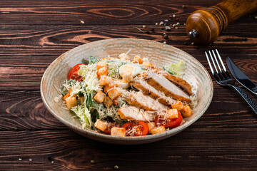 Italian food Caesar salad with chicken, parmesan cheese, lettuce, eggs, tomatoes, croutons on a wooden table.