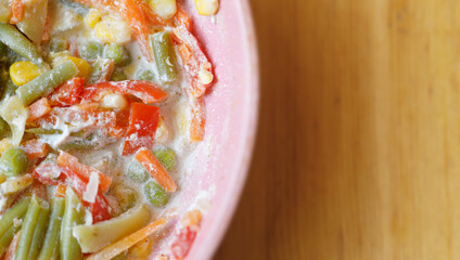 Top angle on a colorful bowl of mixed frozen vegetables on a wooden surface