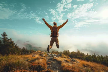Fotobehang A happy man jumping from a mountainside with his arms raised  a successful hiker enjoying his accomplishments on a cliff  an idea of a life with a young man climbing a woodland walk. © ProDesigner
