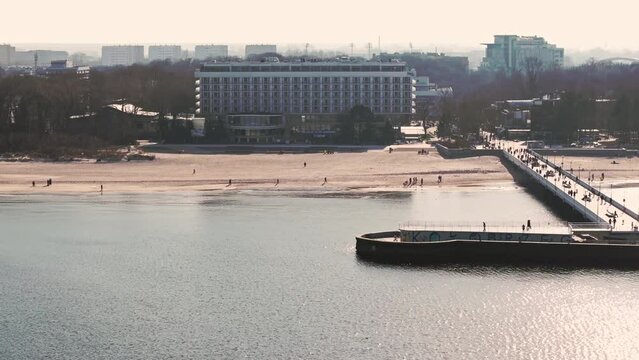 Kołobrzeg pier on a sunny February afternoon. Windless weather, calm sea without a single wave, tourists strolling on the pier.