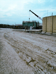 A crane is lifting a large object in a construction site. The crane is positioned near a building and a sign is visible in the background.