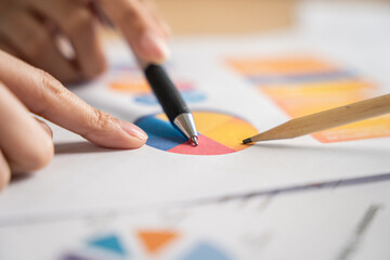 Close-up of a professional analyzing statistical data on a colorful pie chart report with a pen and...