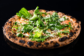 Italian cuisine pizza with chicken, cheese, tomatoes, arugula, lettuce and spices on black.