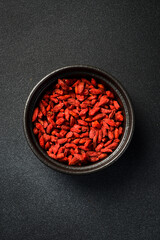 Close up of red dried goji berries in a bowl. On a dark concrete background.