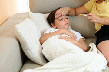 Sick child on the couch at home. Someone puts their hand on the child's forehead and looks at the thermometer