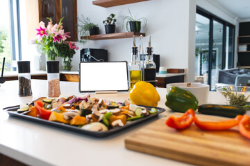 A tablet with a blank screen stands among various cooking ingredients on a kitchen counter