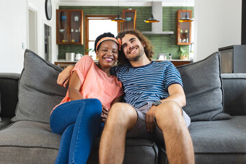 Diverse couple young African American woman and Caucasian man sit closely on a sofa, smiling warmly