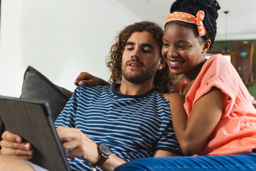 Diverse couple young Caucasian man and African American woman share a tablet, cozy on a couch