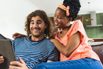 Diverse couple young African American woman and young Caucasian man share a tablet, smiling together