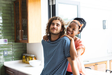 Diverse couple young African American woman embraces a young Caucasian man in a cozy kitchen