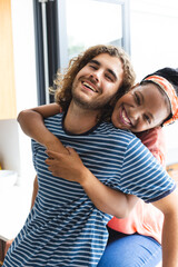 Diverse couple young African American woman embraces a young Caucasian man from behind, both smiling