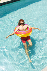 Young Caucasian man with curly hair relaxes on a colorful float in a pool with copy space
