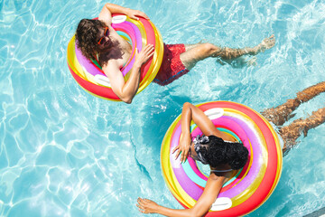 A diverse couple, a young Caucasian man and an African American woman relax on colorful pool floats