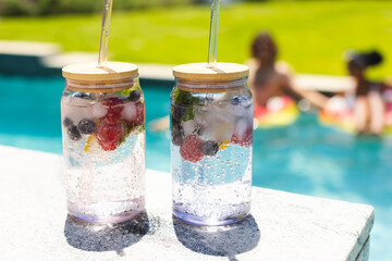 Two refreshing fruit-infused water jars with straws sit by a pool