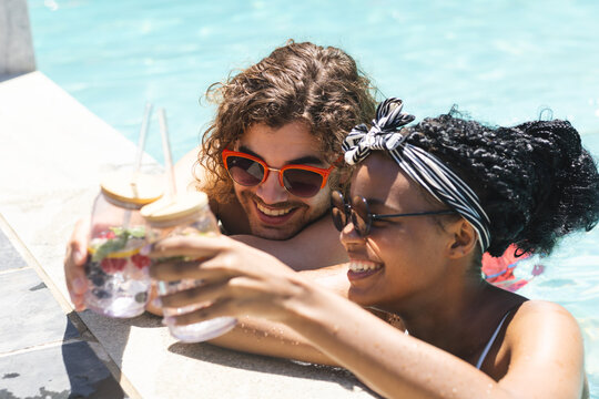 Diverse couple enjoying drinks by the pool, the woman's hair adorned with a headband - Powered by Adobe