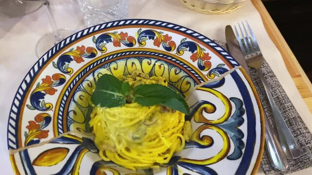 Traditional Italian restaurant with tasty original carbonara pasta on decorated plate, spaghetti with fresh egg yolk, grated pecorino cheese, black pepper and fresh menthol leaves, delicious lunch or