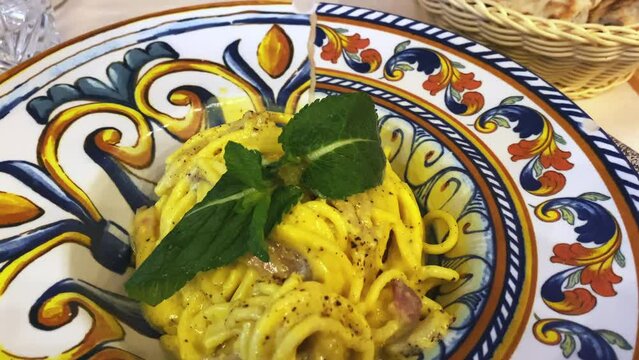 Italian carbonara pasta on traditional decorated plate, spaghetti with fresh egg yolk, grated pecorino cheese, black pepper and fresh menthol leaves, delicious Italian lunch or dinner in local