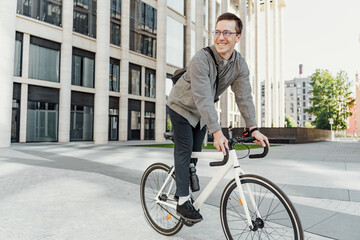 Joyful man cycling on urban bike in smart casual wear, with modern buildings behind.