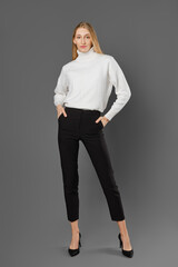 Slender tall woman in tight breeches and a sweater posing in the studio on a grey background
