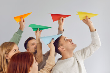 Joyful group of young people enthusiastically launching colorful paper airplanes into air. Smiling...