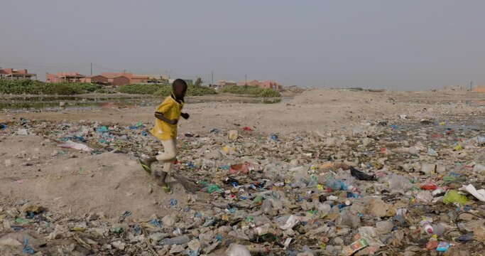 Slow motion. Young Black African boy playing amongst horiffic plastic pollution.