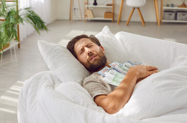 Man sleeping with money savings on his chest. Bearded man lying on white pillow on couch with bunch...