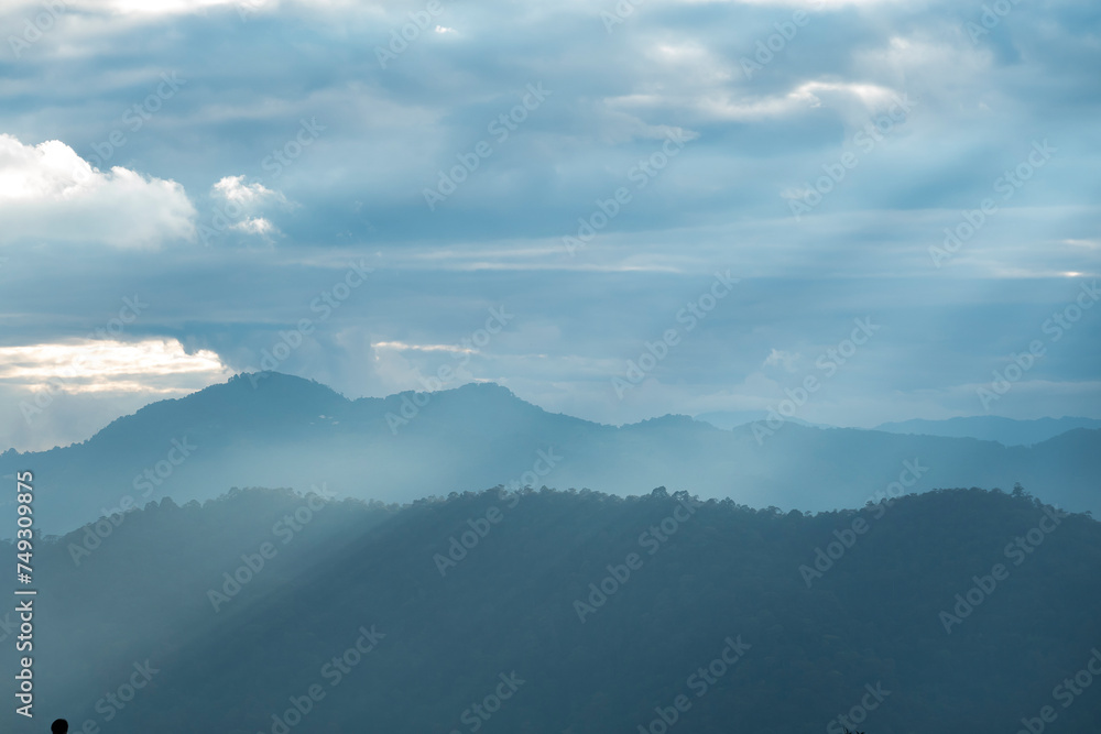 Wall mural sun rays filter through the clouds in hills of the valley illuminated by the sun's rays filtering th
