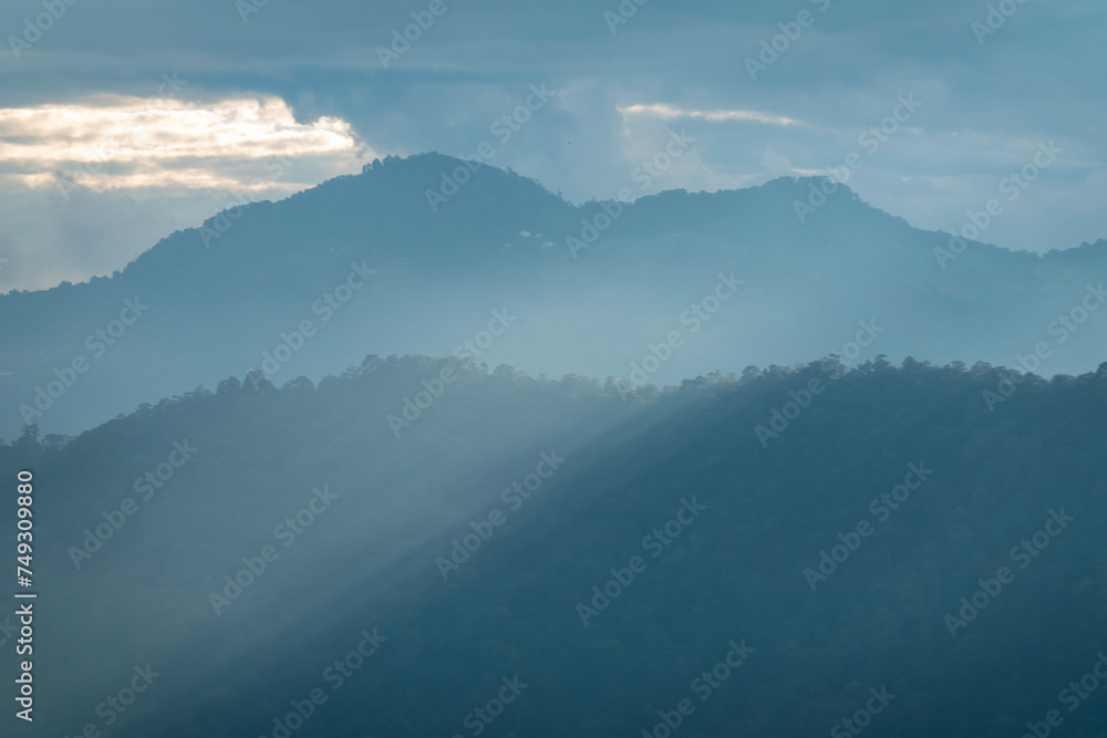 Wall mural sun rays filter through the clouds in hills of the valley illuminated by the sun's rays filtering th